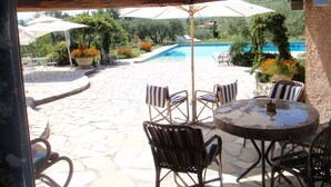 Une terrasse extérieure avec un sol en pierre, des chaises à rayures, une table ronde et des parasols.