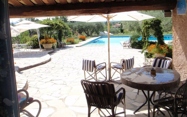 Un patio al aire libre con piso de piedra, sillas a rayas, una mesa redonda y sombrillas.