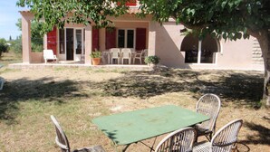 Une maison dotée d’un patio comprenant une table et des chaises, un pot de fleurs et une porte rouge.