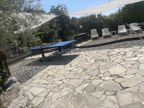 Een terras van natuursteen met buitenmeubels en een tafeltennistafel.