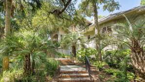 A house with a brick staircase leading to a porch surrounded by lush greenery.