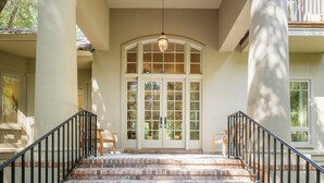 A grand entrance with a large arched doorway, a staircase with black railings, and a hanging light fixture.
