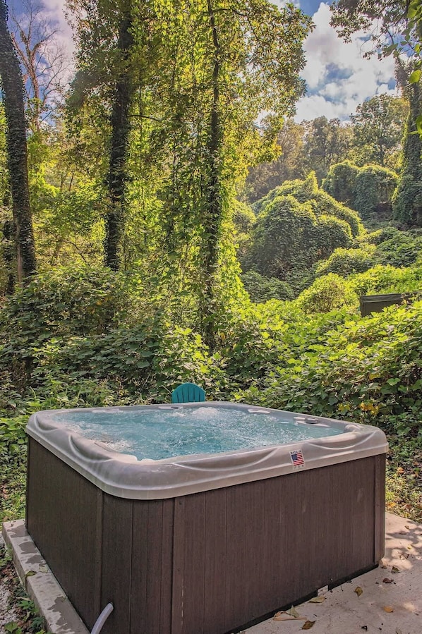 A hot tub in a lush garden with dense foliage and trees in the background.