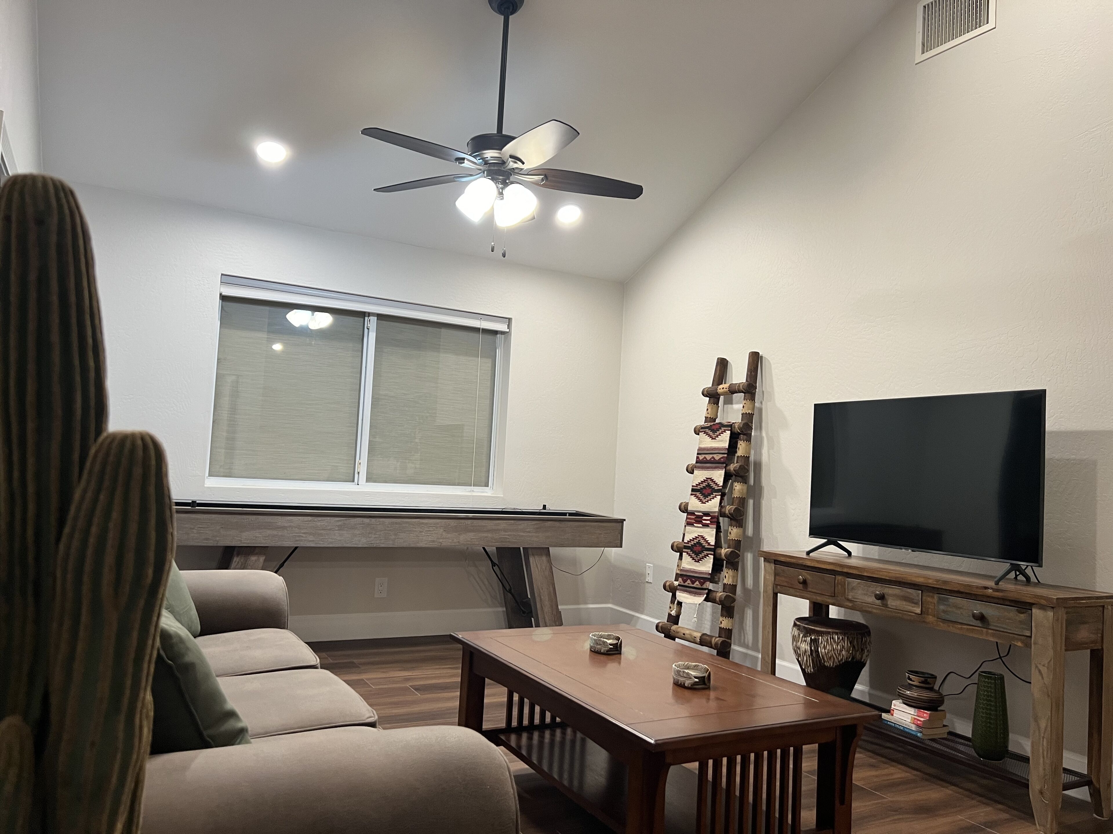 A living room with a ceiling fan, a television, a wooden table, and a window.