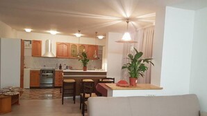 A modern living room with a sofa, a dining area with chairs, a kitchen with wooden cabinets, and a ceiling fan. - Beautiful 3-bedroom apartment with lake view (Radovljica)