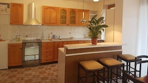 A modern kitchen with wooden cabinets, a stainless steel oven, a sink, and a bar area with stools. - Beautiful 3-bedroom apartment with lake view (Radovljica)