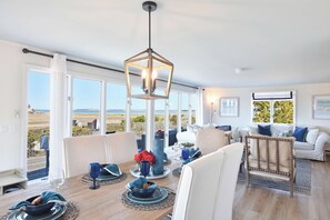 A spacious living room with a dining area, large windows, and a view of the outdoors. - Dreamy Water Views w/ Central AC (Eastham)