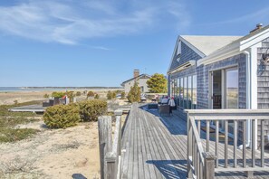 A coastal property with a wooden deck, a glass-enclosed room, and a view of the beach. - Dreamy Water Views w/ Central AC (Eastham)