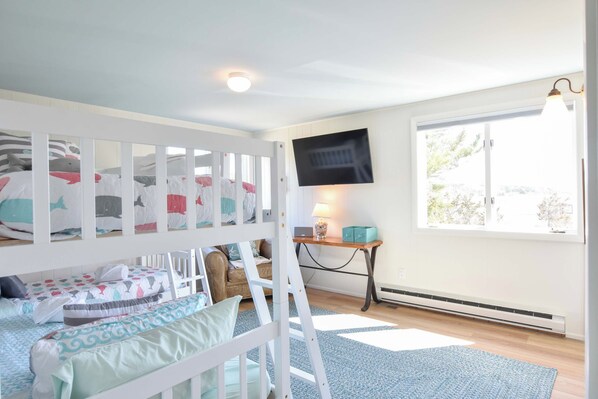 Une chambre d’enfant avec des lits superposés, une télévision, un bureau et une fenêtre donnant sur un beau paysage.