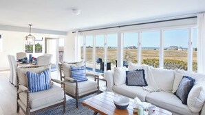 A spacious living room with a large window offering a view of the beach and ocean.