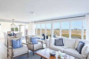 A spacious living room with a large window offering a view of the beach and ocean.