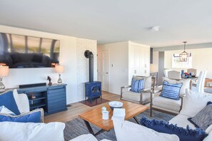 A living room with a fireplace, seating, and a television. - Dreamy Water Views w/ Central AC (Eastham)