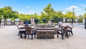 Une terrasse extérieure avec un foyer en pierre, des fauteuils Adirondack et un espace barbecue.