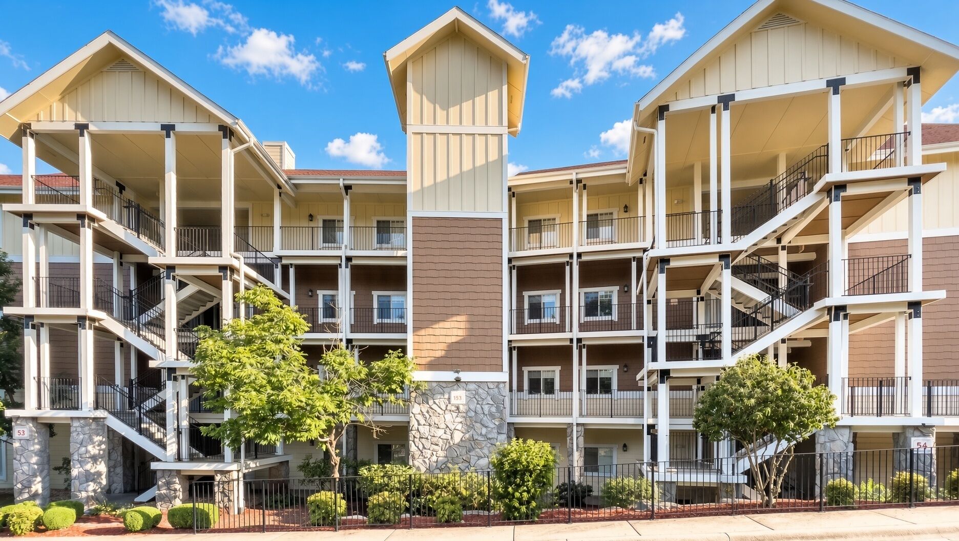 A multi-story residential building with balconies, a stone facade, and a clear sky.