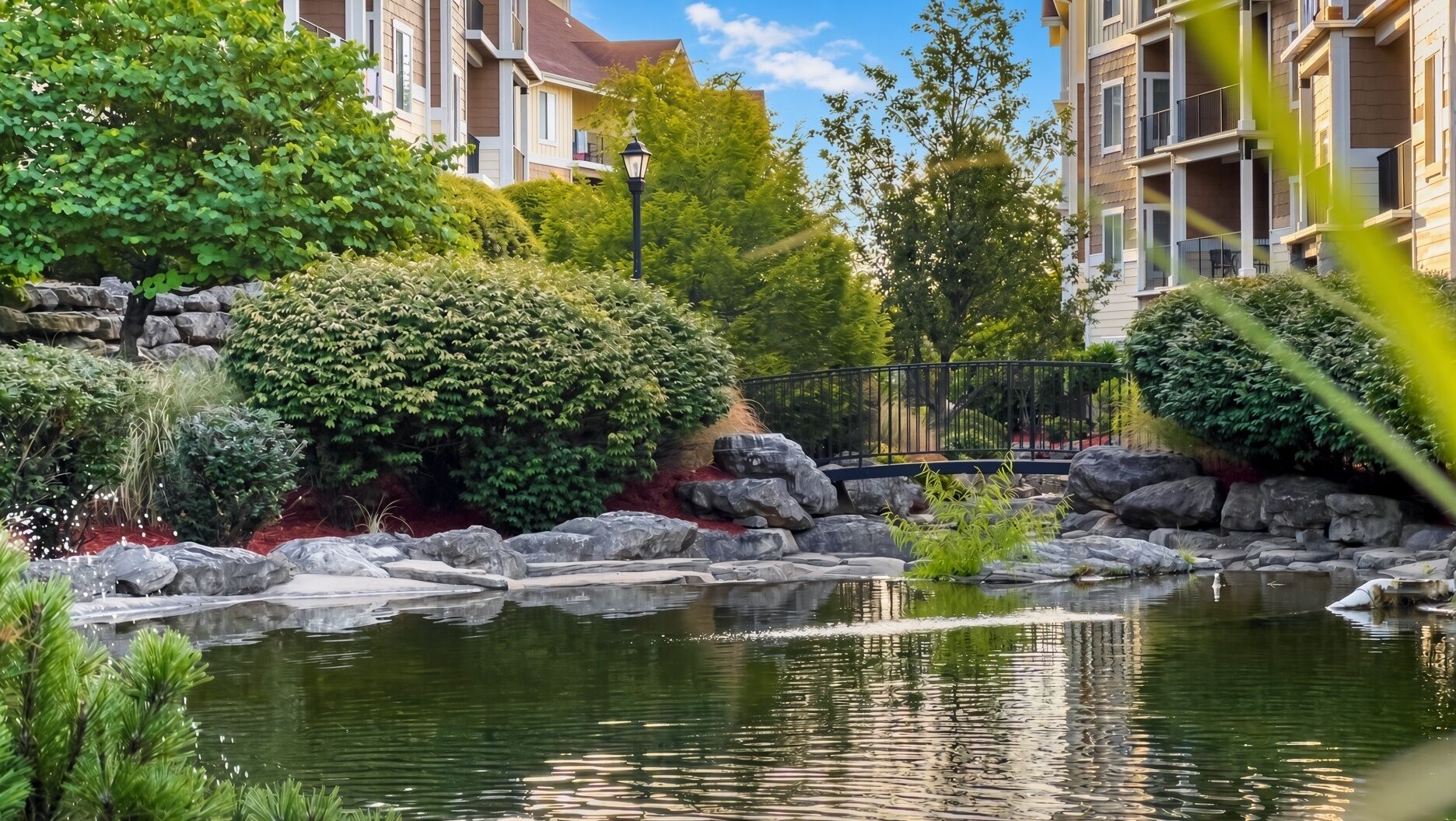 A residential area with a pond, greenery, and multi-story buildings.