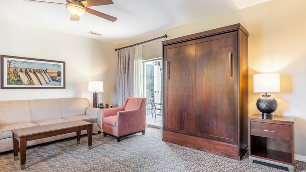 A hotel room with a sofa, armchair, wooden wardrobe, bedside table, lamp, and a painting on the wall. - Branson | Pool & Mountains | Scenic Ozark Stay (Banson)