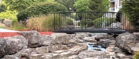 A landscaped area with a stone waterfall, a metal bridge, and a red mulch border.