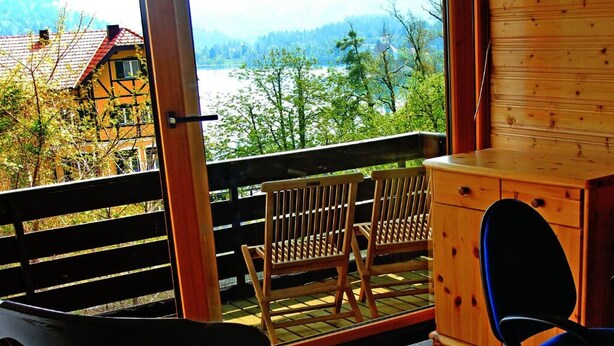 A wooden balcony with a view of a lake and mountains, a wooden chair, and a small wooden cabinet. - Beautiful house with lake view, for large groups! (Radovljica)