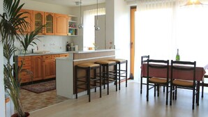 A modern kitchen with wooden cabinets, a central island with stools, and a dining area with a table and chairs. - Beautiful house with lake view, for large groups! (Radovljica)