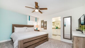 Un dormitorio con cama, ventilador de techo, mesita de noche, lámpara y vistas al baño.