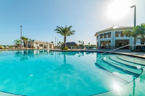 Piscina azul cristalina con borde curvo, rodeada de palmeras y un edificio con múltiples ventanas.
