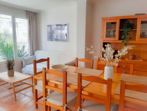 Zona pranzo con tavolo e sedie in legno, un divano bianco e un mobile con ante in vetro.