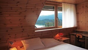A bedroom with a bed, a desk, and a window with a view of a lake and mountains.