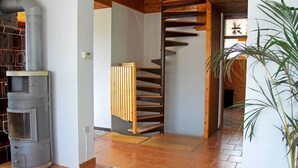 A modern interior with a wood-burning stove, a spiral staircase, and a potted plant.