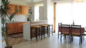 A modern kitchen with wooden cabinets, a central island with stools, and a dining area with a table and chairs.