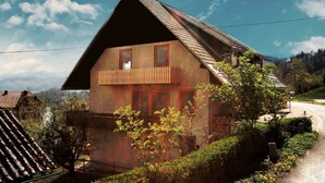 A traditional chalet with a sloped roof, a wooden balcony, and a view of a rural landscape.