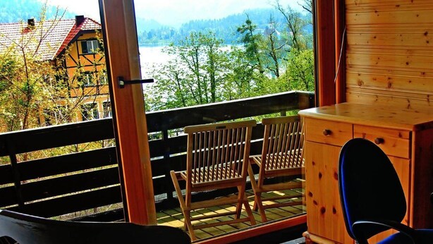 A balcony with wooden chairs, a small wooden cabinet, and a view of a lake and buildings.