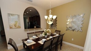Une salle à manger avec une longue table dressée pour six personnes, un lustre et un miroir décoratif au mur.
