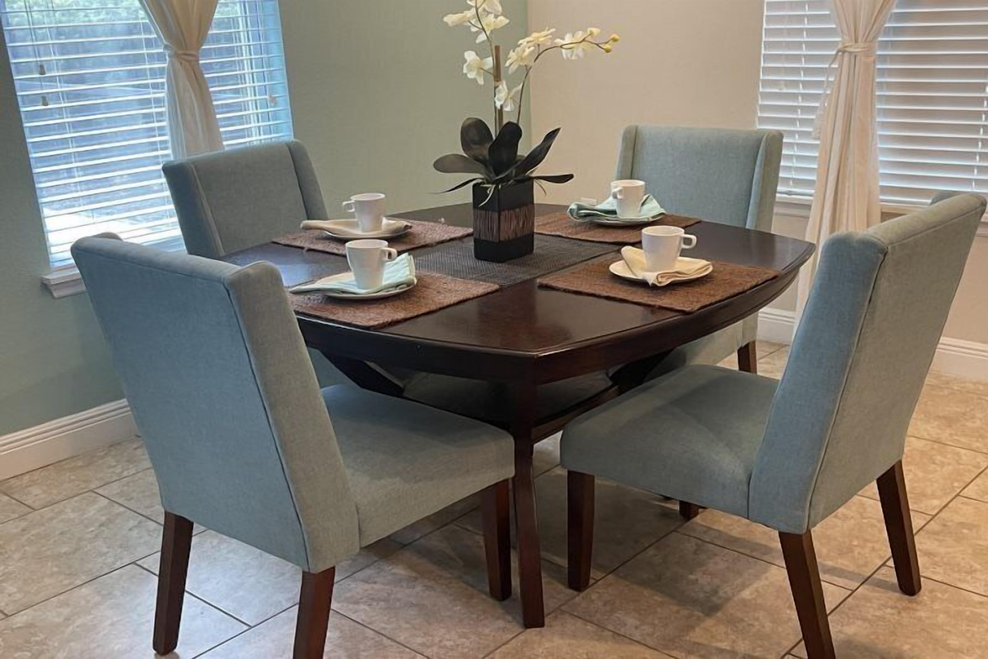 A dining table with four chairs, a vase with flowers, and a set of cups and saucers.