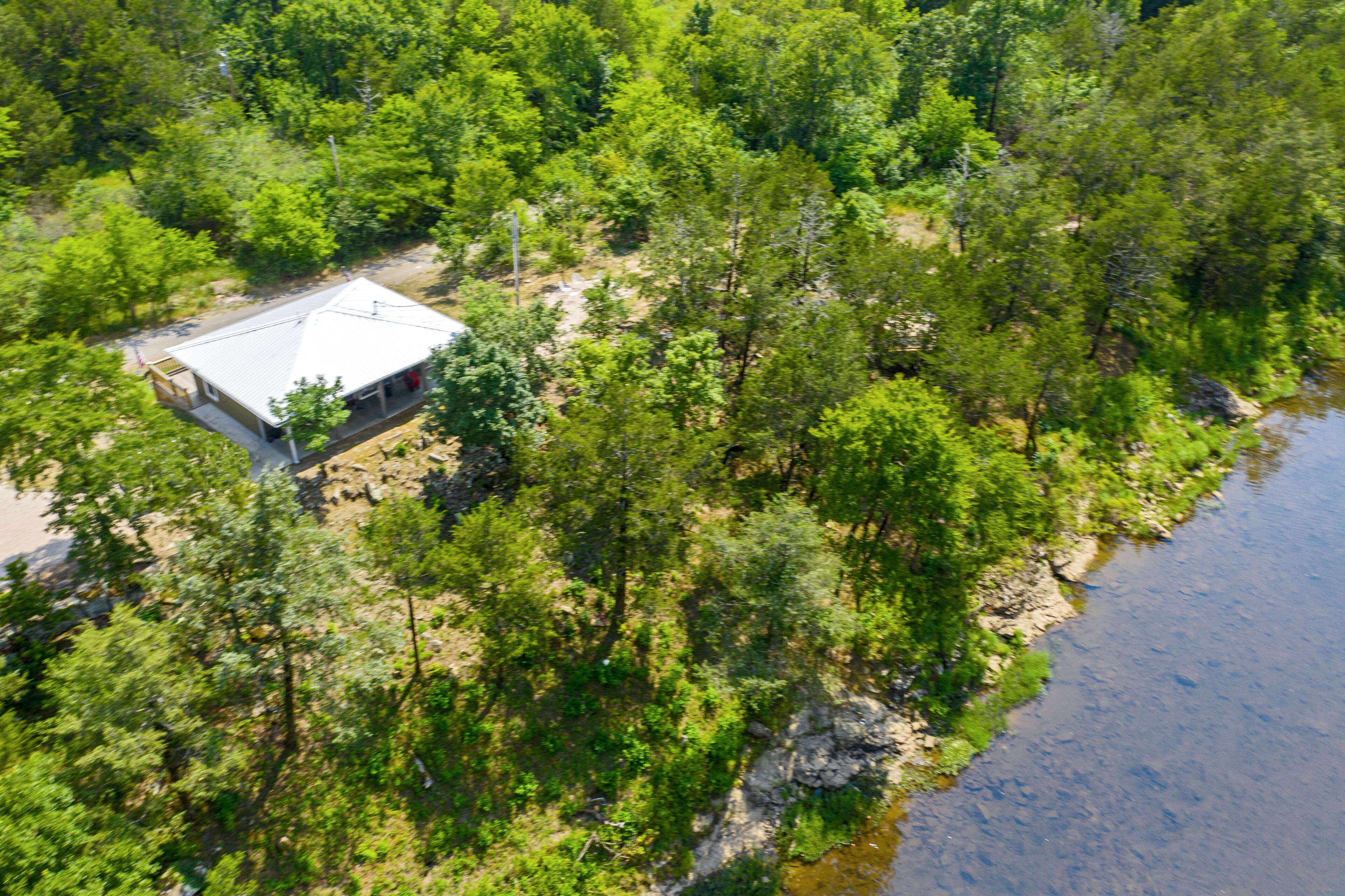 An aerial view of a cabin surrounded by dense forest and a river.