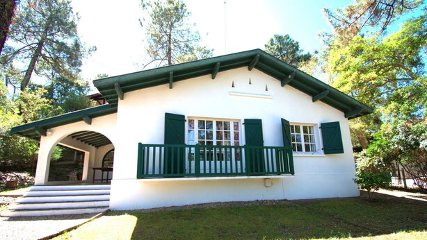 A white building with green shutters and a porch, surrounded by trees. - Hossegor "ENEA" Pleasant villa for 6 people. (HOSSEGOR)