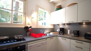A kitchen with white cabinets, a stove, a dishwasher, and a window with a view of greenery outside. - Hossegor "ENEA" Pleasant villa for 6 people. (HOSSEGOR)