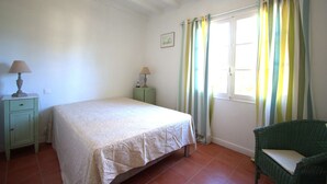 A bedroom with a bed, a nightstand, a lamp, a chair, a window with curtains, and a picture on the wall. - Hossegor "ENEA" Pleasant villa for 6 people. (HOSSEGOR)