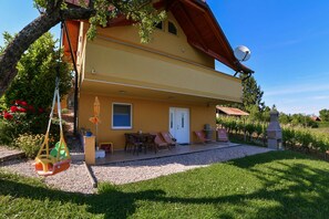 Un edificio de dos pisos con un patio, mobiliario exterior y un jardín.
