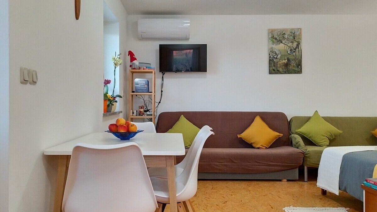 Un espacio habitable compacto con sofá, mesa de comedor y televisor montado en la pared.