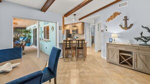 A spacious kitchen with wooden cabinets, a dining area with blue chairs, and a view into a living room with a pool. - Sunny Cape Coral Pool Home (Cape Coral)