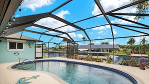 A swimming pool with a clear blue water feature, surrounded by a covered area with metal beams and string lights. - Sunny Cape Coral Pool Home (Cape Coral)