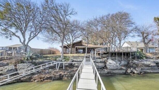 A wooden bridge leading to a building with a deck, surrounded by trees and a pond. - The Lake Shack-----Water Front!!! (Brownwood)