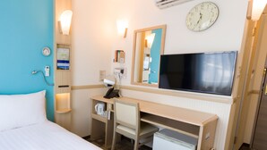 A hotel room with a bed, a desk, a chair, a small refrigerator, a television, a clock, and a mirror.