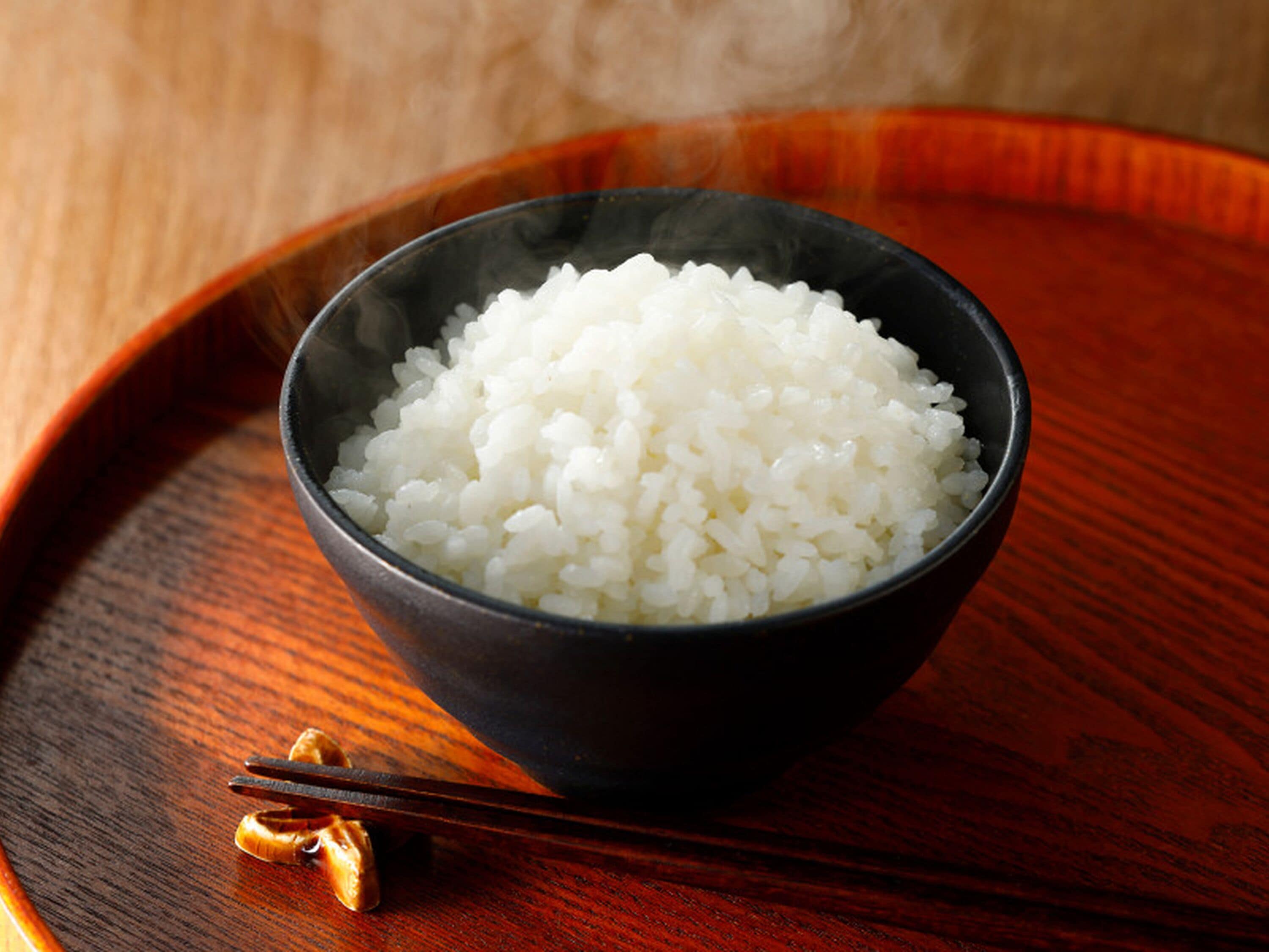 Uma tigela de arroz branco sobre um tabuleiro de madeira.