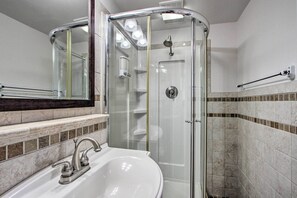 Un bagno moderno con cabina doccia in vetro, lavandino bianco e specchio sopra il lavandino.