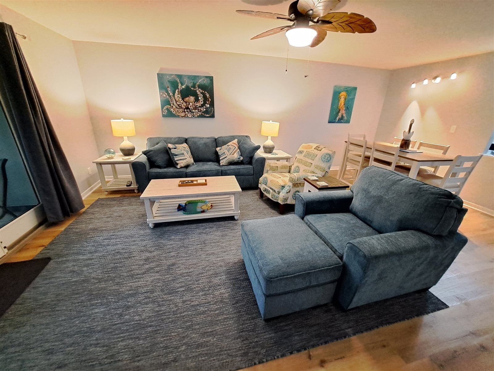 A living room with a sofa, armchair, coffee table, and a ceiling fan.