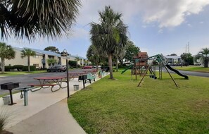 A park with picnic tables, a playground, and a building in the background. - Seascape #1101 Newly Renovated Beach Service Included 2 Chairs and Umbrella (DESTIN)