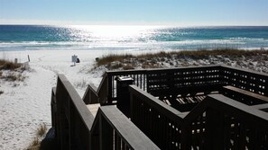 Een houten looppad leidt naar een zandstrand met een helder uitzicht op de oceaan.