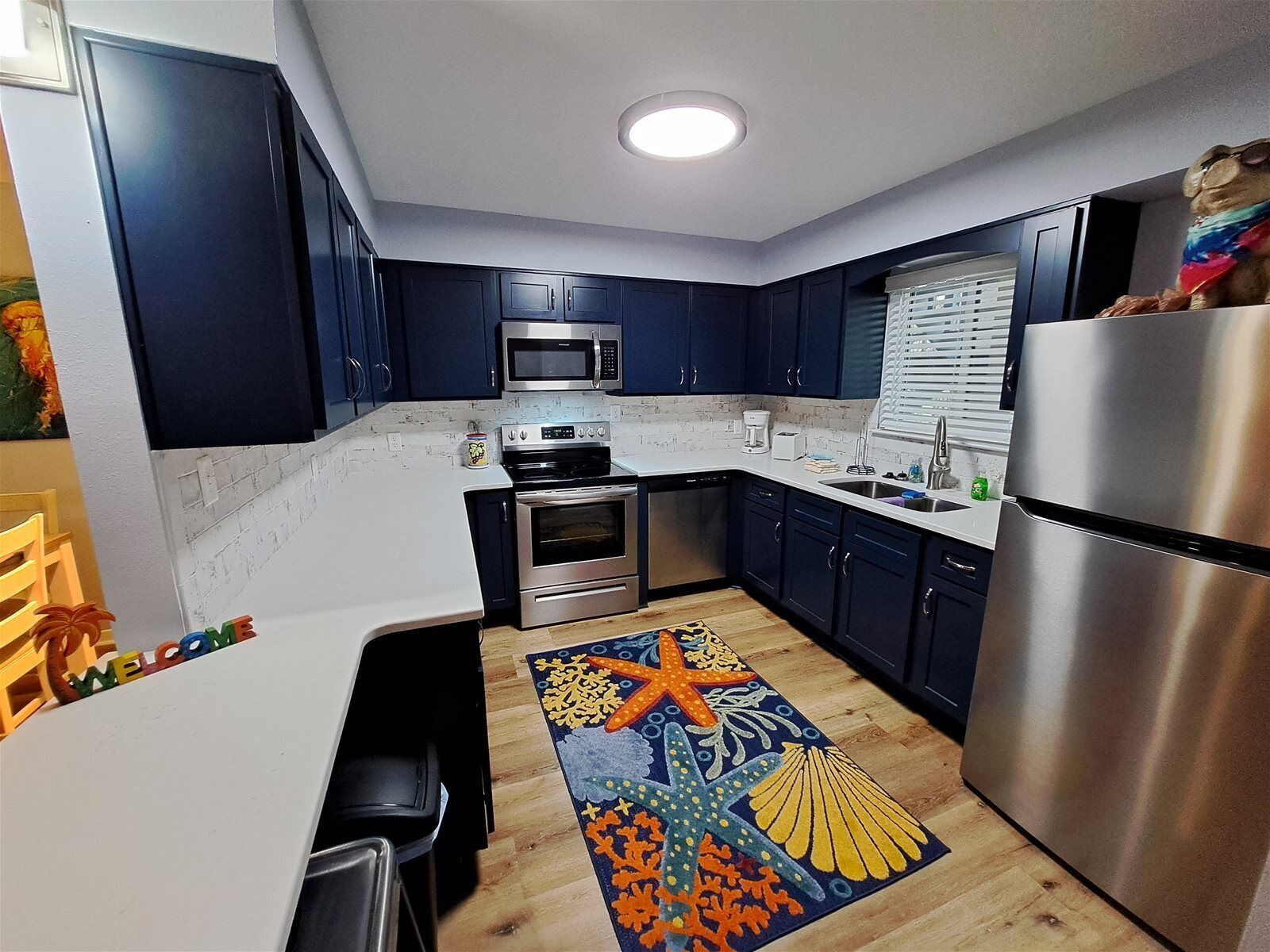 Een moderne keuken met donkerblauwe kastjes, roestvrijstalen apparatuur en een kleurrijk vloerkleed.