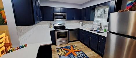 Een moderne keuken met donkerblauwe kastjes, roestvrijstalen apparatuur en een kleurrijk vloerkleed.